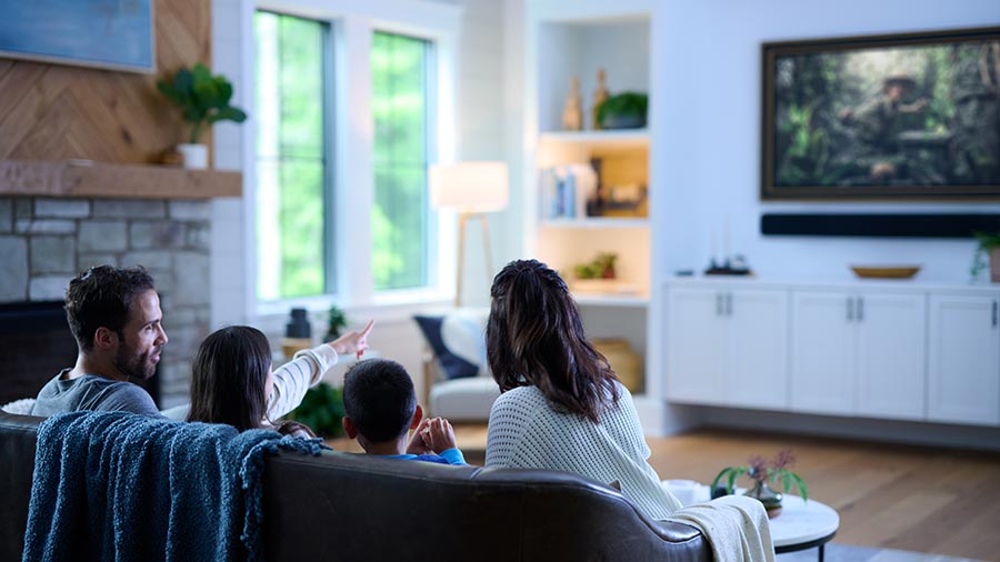 Family sitting on a couch watching video content across multiple screens